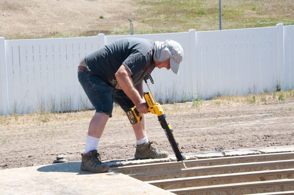 Volunteer Tom Putting Down Subfloor Adhesive at the Build Site.