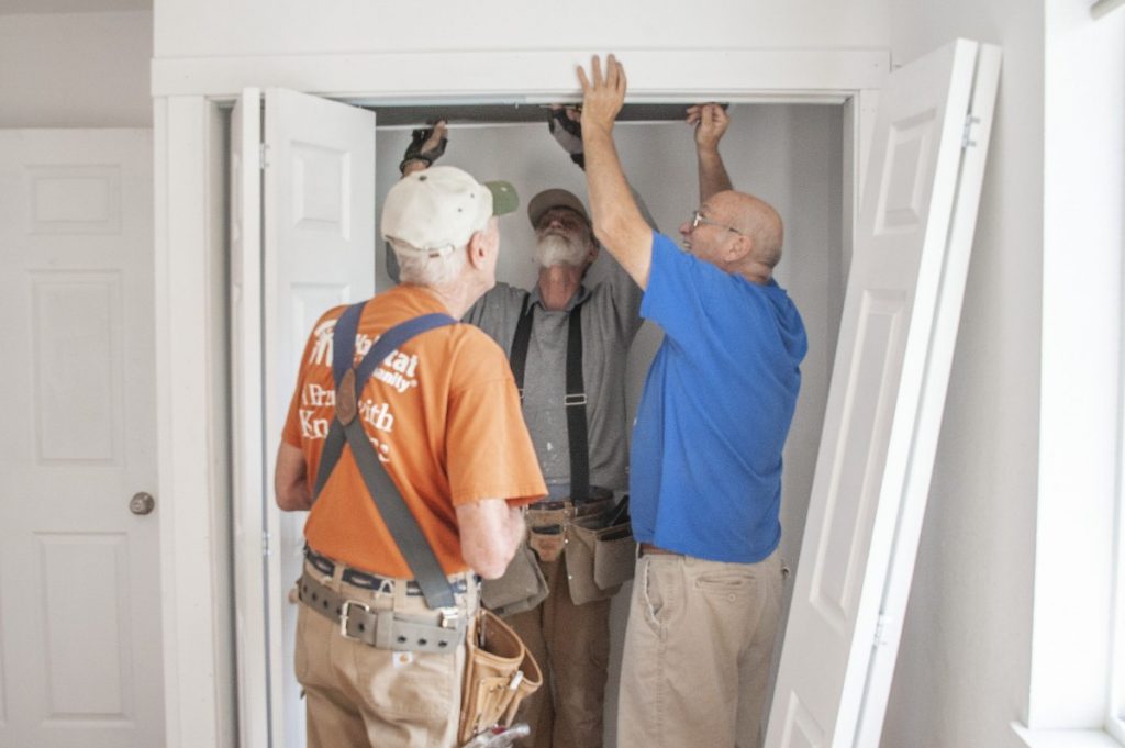 Three volunteers work to install closet doors at the build site.