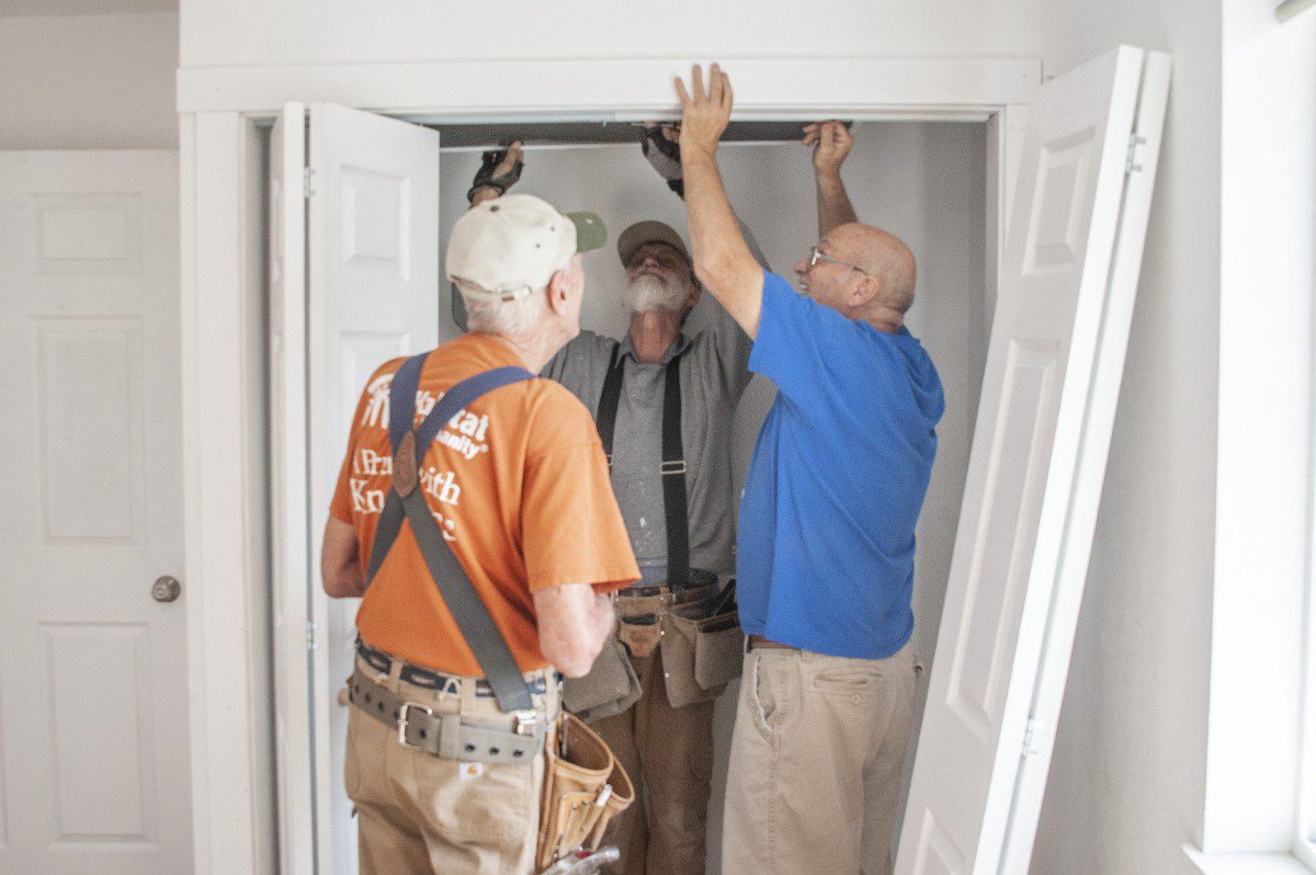 Three volunteers work to install closet doors at the build site.