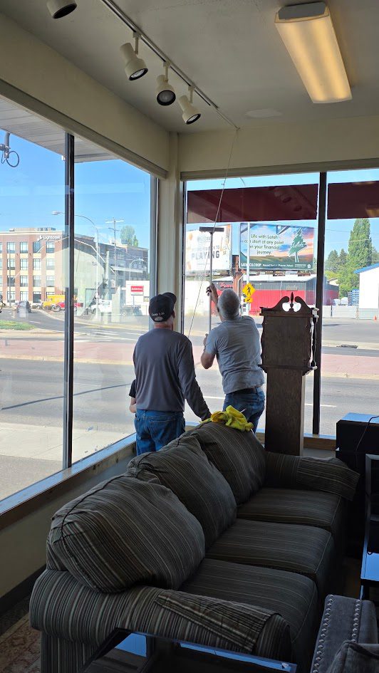 Two members of The 226 Men working together to reach the tall windows in the ReStore's furniture section